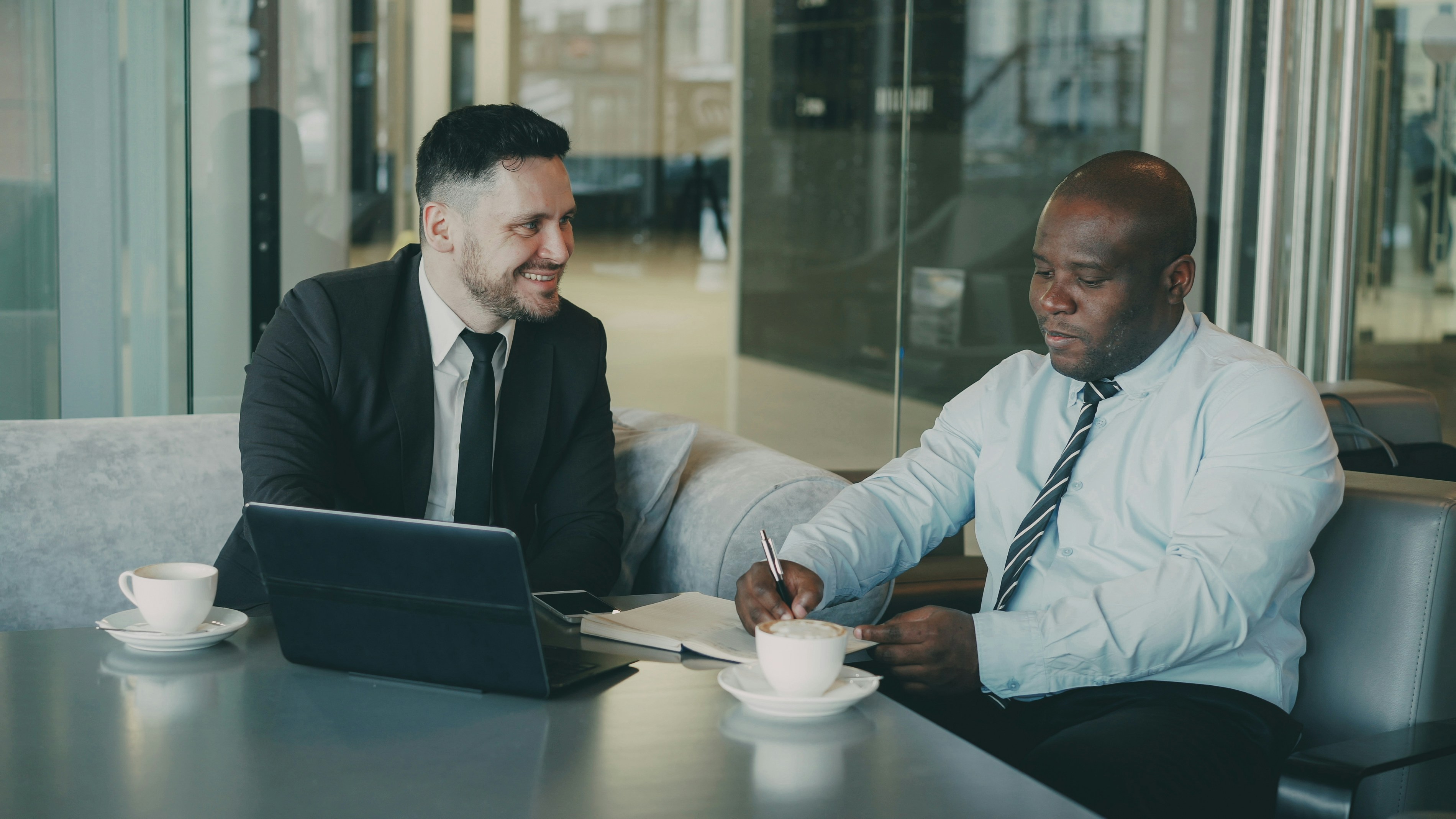 Two ambitious business partners looking through their contract and singing it at their table with laptop and graphs in airy cafe.